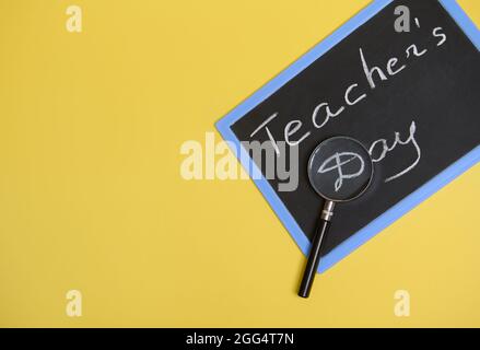 Composition à plat à partir d'une loupe, d'une loupe, d'une lentille, d'une loupe sur un tableau noir avec lettrage Teachers Day sur fond jaune avec espace de copie Banque D'Images