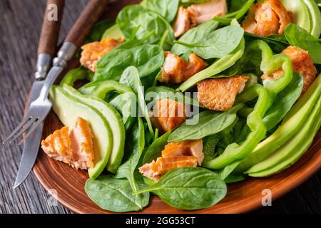 salade de saumon à l'avocat aux épinards et au poivre vert sur une assiette rustique brune avec fourchette et couteau sur une table en chêne tourbière, alimentation saine méditerranéenne, gros plan Banque D'Images