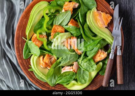 saumon épinards avocat et salade de poivre vert sur une assiette rustique brune avec fourchette et couteau sur une table en chêne tourbière, régime méditerranéen sain, plat, cl Banque D'Images