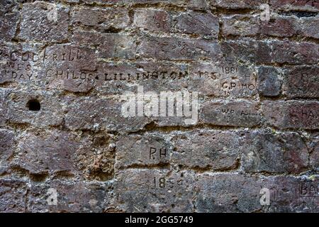 Vieux graffiti, principalement du XIXe siècle, sculpté dans la brique de la tour sud-est de l'intérieur du château de Portchester bailey: Portchester, Hampshire, Royaume-Uni Banque D'Images