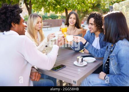 Groupe multiethnique d'amis qui toaster avec leurs boissons tout en prenant un verre ensemble. Banque D'Images