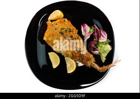 plaque noire avec poisson-de-mer pané sur fond blanc Banque D'Images