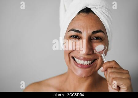 Femme âgée qui fait des soins de la peau en utilisant le rouleau de visage - foyer principal sur les yeux Banque D'Images