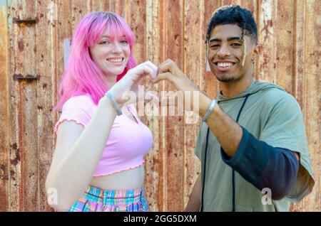 autre couple divers se traînant ensemble en souriant et debout contre un mur rouillé de fond et tenant les mains en forme de coeur. amis heureux Banque D'Images