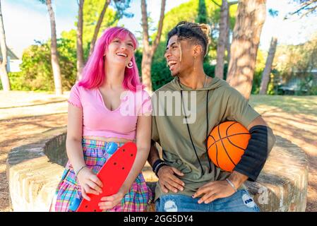 autre couple divers qui se traînait ensemble, se détend dans un parc où se tiennent un basket-ball et un skateboard. des amis interraciaux heureux Banque D'Images