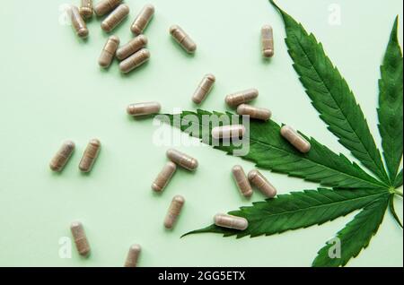 Pilules de CBD. Groupe de capsules claires de cannabis CBD et de feuille de chanvre sur fond vert Banque D'Images