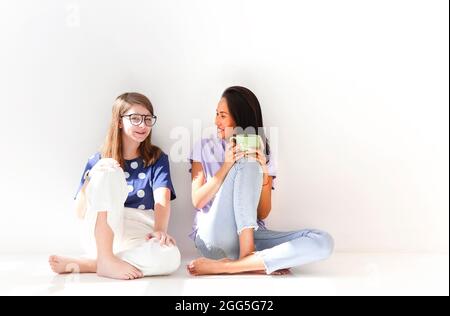 Deux joyeuses femmes décontractées se détendant avec une boisson chaude dans la nouvelle maison. Jeunes filles discutant parler de choses drôles ragots riant dans l'appartement lumineux. Femme Banque D'Images