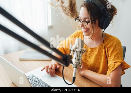 Une femme joyeuse hôte diffuse son podcast à l'aide d'un microphone vocal. Une femme qui fait du podcaster un flux audio dans son petit studio Banque D'Images