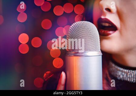 Chanteuse avec microphone disco sur fond bokeh. Gros plan des lèvres pour femmes peintes avec un rouge à lèvres bordeaux et un microphone rétro. REDHEAD fille débutant le concert. Espace de copie pour les affiches de concert. Banque D'Images