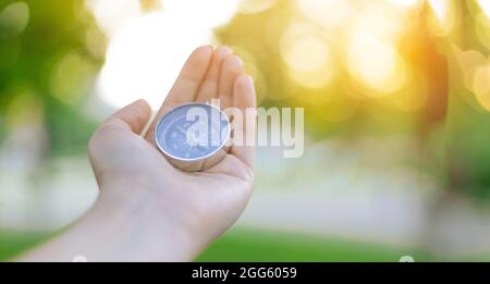 Personne main avec boussole sur fond vert flou avec le soleil éblouissant au coucher du soleil ciel Banque D'Images