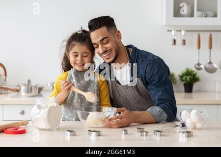 Joyeux papa arabe et sa petite fille préparant la pâte pour la pâtisserie ensemble Banque D'Images