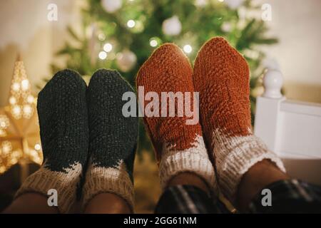 Couples pieds dans des chaussettes en laine confortables sur fond d'arbre de noël dans des lumières dans la salle de soirée festive. Célébrez ensemble les vacances d'hiver, en famille Banque D'Images