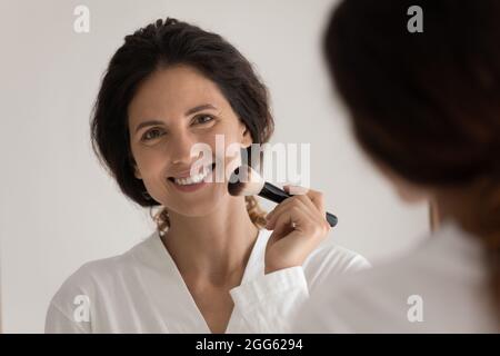 Jeune femme hispanique souriante se maquillant à la maison. Banque D'Images