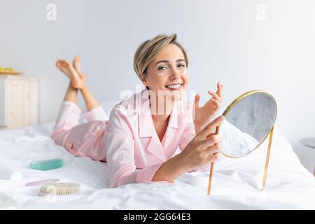 Portrait d'une femme souriante tenant un miroir appliquant de la crème Banque D'Images