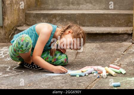 Petit enfant d'âge scolaire dessin avec de la craie sur le béton assis au sol. Art thérapie, intégration sensorielle concept simple. arti. Créative Banque D'Images