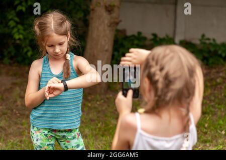 Deux jeunes enfants en bas âge, des enfants en âge d'aller à l'école utilisant des gadgets électroniques, des enfants et de la technologie tourné en plein air. Bracelet Smart Fit et smartphone pour prendre des photos Banque D'Images