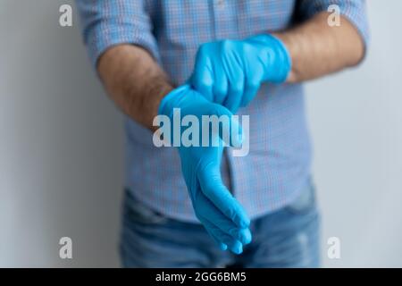 Homme portant des gants en latex de caoutchouc bleu pour le travail à domicile Banque D'Images