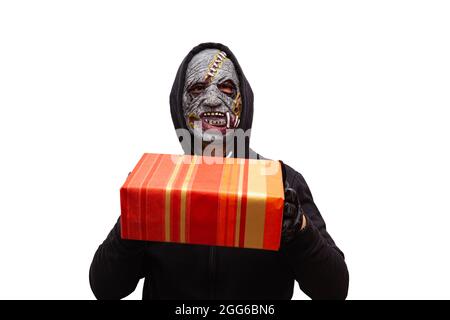 Un homme déguisé dans un masque zombie portant un sweat-shirt à capuche noir tient un paquet de cadeau dans ses mains prêtes au livrer à quelqu'un. Banque D'Images