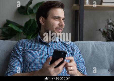 Un utilisateur de téléphone portable attentionné et positif assis sur le canapé à la maison Banque D'Images