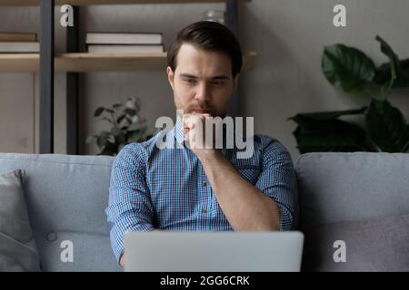 Jeune homme millénaire concentré regardant ou lisant du contenu multimédia en ligne Banque D'Images