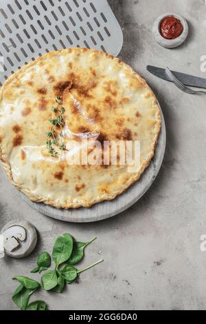 Pizza italienne calzone avec mozzarella, jambon, basilic sur plateau rond en marbre, garniture en pierre grise avec ingrédients pour pizza Banque D'Images