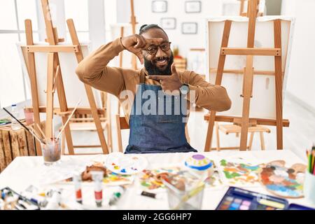 Artiste afro-américain homme au studio d'art souriant faisant cadre avec les mains et les doigts avec le visage heureux. Créativité et concept de photographie. Banque D'Images