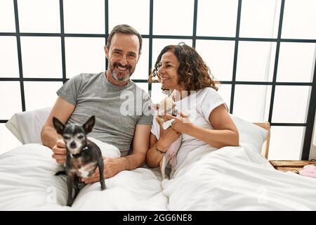 Couple hispanique d'âge moyen souriant heureux couché sur le lit avec des chiens à la maison. Banque D'Images