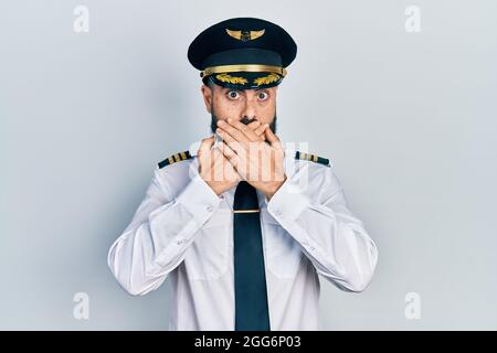 Un jeune homme hispanique portant un uniforme de pilote d'avion a choqué la bouche avec des mains pour erreur. Concept secret. Banque D'Images