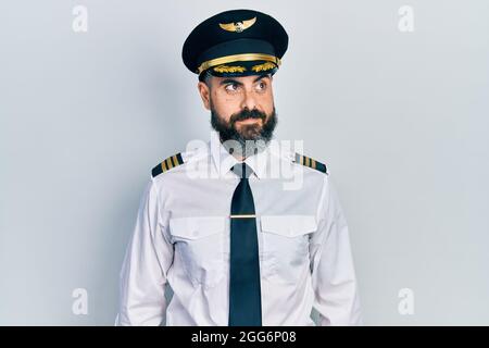 Jeune homme hispanique portant l'uniforme de pilote d'avion souriant regardant sur le côté et regardant loin de penser. Banque D'Images