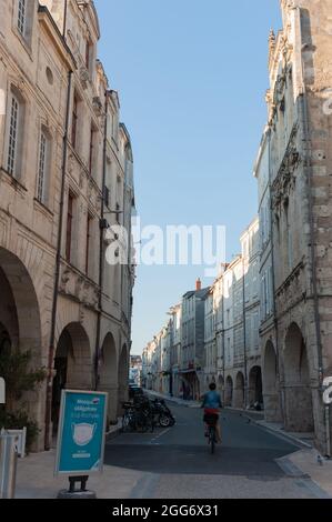 La Rochelle, France; 10 août 2021: Cycliste le long d'une rue avec un panneau au début du port obligatoire des masques dans le ce historique Banque D'Images