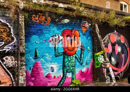 ESPACE ARTISTIQUE ET CULTUREL DE LONDRES AUTOUR DE LA RUELLE DE BRIQUES AVEC DES MOTIFS CRÉATIFS ET DES SLOGANS COLORÉS MUR AVEC HERBE ET FLEURS Banque D'Images