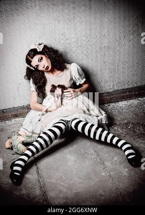 Étrange fille solitaire avec des poupées assis dans une pièce sale Banque D'Images