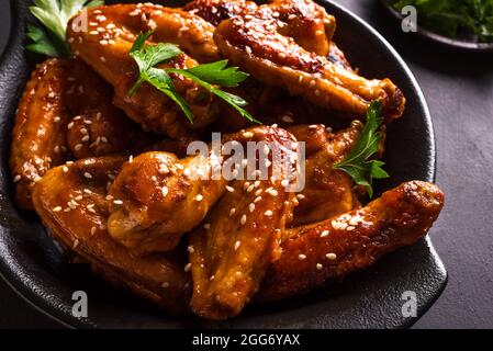 Ailes de poulet teriyaki au sésame et aux verts sur fond noir. Repas de style asiatique - ailes de poulet rôties avec sauce teriyaki. Banque D'Images