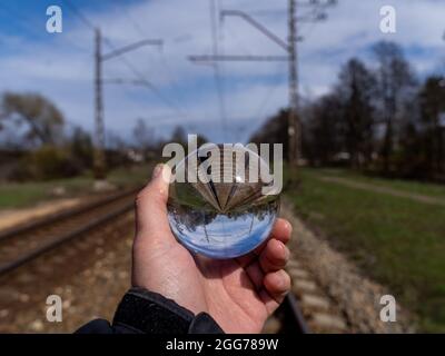 Boule de verre avec voies de chemin de fer visibles UNE boule de verre tenue dans la main d'un homme se tient sur les voies de chemin de fer. Une boule de verre les pieds visibles dans l'air à l'envers Banque D'Images