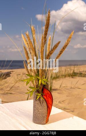 Un vase en céramique d'argile et une tasse avec une soucoupe placée sur une nappe de lin sur la plage de la mer. Les parties inférieures du vase et de la tasse sont une couche de gros Banque D'Images