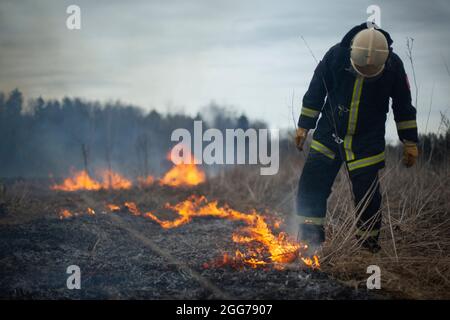 Un pompier éteint l'herbe sèche. Un pompier lutte contre un incendie dans une zone ouverte. Mesures de secours contre les flammes. Une catastrophe écologique brûlée Banque D'Images