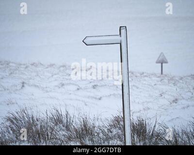 Sortie blanche - panneau de chemin de pied avec montant à doigts et panneau de route triangulaire oblitéré par la neige sur les landes dans la tempête d'hiver Cumbria, Angleterre, Royaume-Uni Banque D'Images