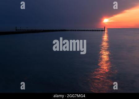 Coucher de soleil depuis la plage de Darłówko, en Pologne. Magnifique paysage marin. Deux yachts et brise-lames en bois à l'horizon. Banque D'Images