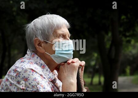 Vieille femme dans un masque de protection assise sur un banc dans le parc. Sécurité pendant la pandémie du coronavirus, la vie à la retraite Banque D'Images