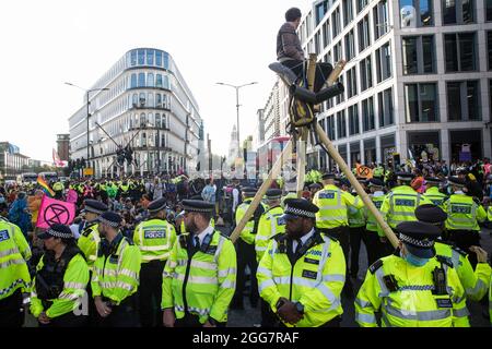 Londres, Royaume-Uni. 27 août 2021. Les militants écologistes de la rébellion d'extinction utilisent trois trépieds pour bloquer une jonction à l'extérieur de la station de métro Mansion House après une marche de l'argent du sang à travers la ville de Londres. Extinction Rebellion avait l'intention de mettre en évidence les institutions financières qui financent des projets de combustibles fossiles, en particulier dans les pays du Sud, ainsi que les cabinets d'avocats et les institutions qui les facilitent, tout en appelant le gouvernement britannique à cesser tous les nouveaux investissements dans les combustibles fossiles avec effet immédiat. Crédit : Mark Kerrison/Alamy Live News Banque D'Images