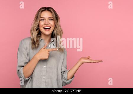 Une jeune femme excitée pointe le doigt sur la paume ouverte pour un nouveau produit ou une vente. Joyeux blonde fille Banque D'Images