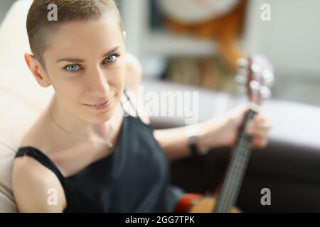 Jeune femme élégante en robe noire jouant ukulele Banque D'Images