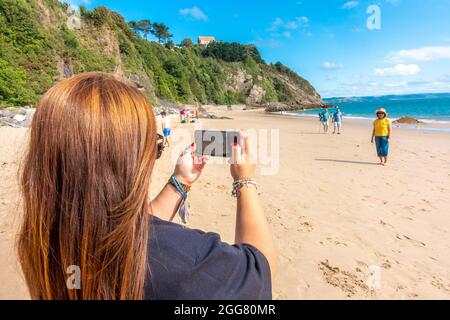 Une dame prend une photo d'un parent à l'aide d'un téléphone portable sur la plage du Nord à Tenby, au pays de Galles. Banque D'Images