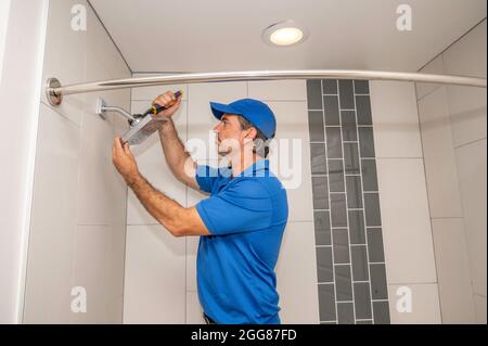 Un plombier travaillant sur une pomme de douche dans une salle de bains moderne Banque D'Images