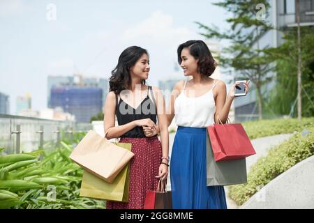 De belles jeunes femmes avec des sacs en papier qui marchent à l'extérieur après avoir fait du shopping ensemble dans le centre commercial local Banque D'Images