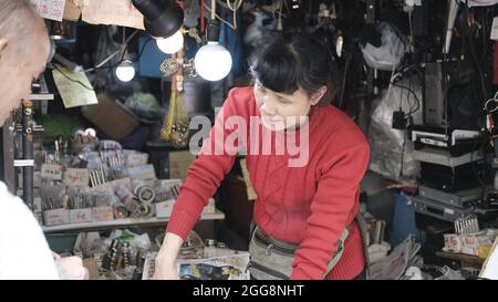 Asian Lady in Red shirt vendant des aimants de matériel au marché de rue Sam Shui po alias le marché d'éclairage de Kowloon, Hong Kong, Chine Banque D'Images