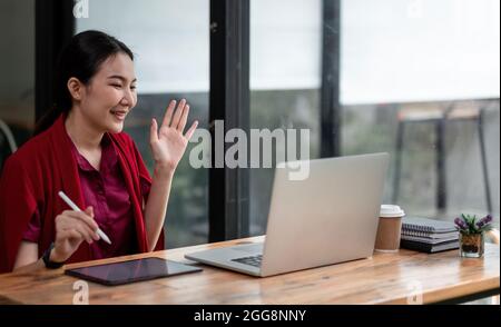 Gros plan photo de positive gaie asiatique fille ont en ligne appel vidéo de diffusion dire hi vague main s'asseoir table utiliser ordinateur portable dans la maison Banque D'Images