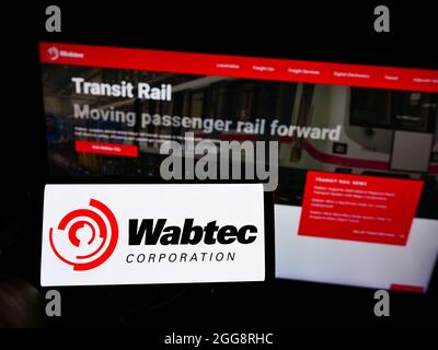 Personne tenant un téléphone portable avec le logo du fabricant de rail américain Wabtec Corporation à l'écran en face de la page Web d'affaires. Mise au point sur l'affichage du téléphone. Banque D'Images