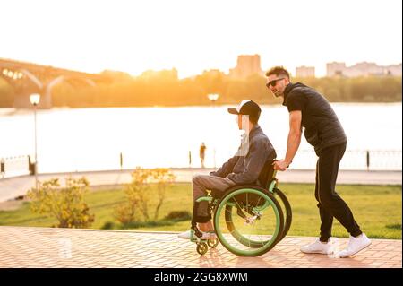 un homme en fauteuil roulant marche avec son ami. Homme marchant avec un ami handicapé en fauteuil roulant au parc Banque D'Images