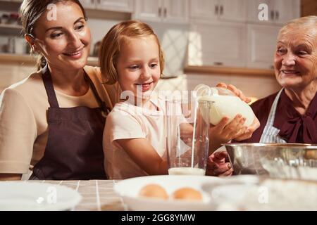 Fière mère et grande fille regardant l'enfant verser du lait Banque D'Images